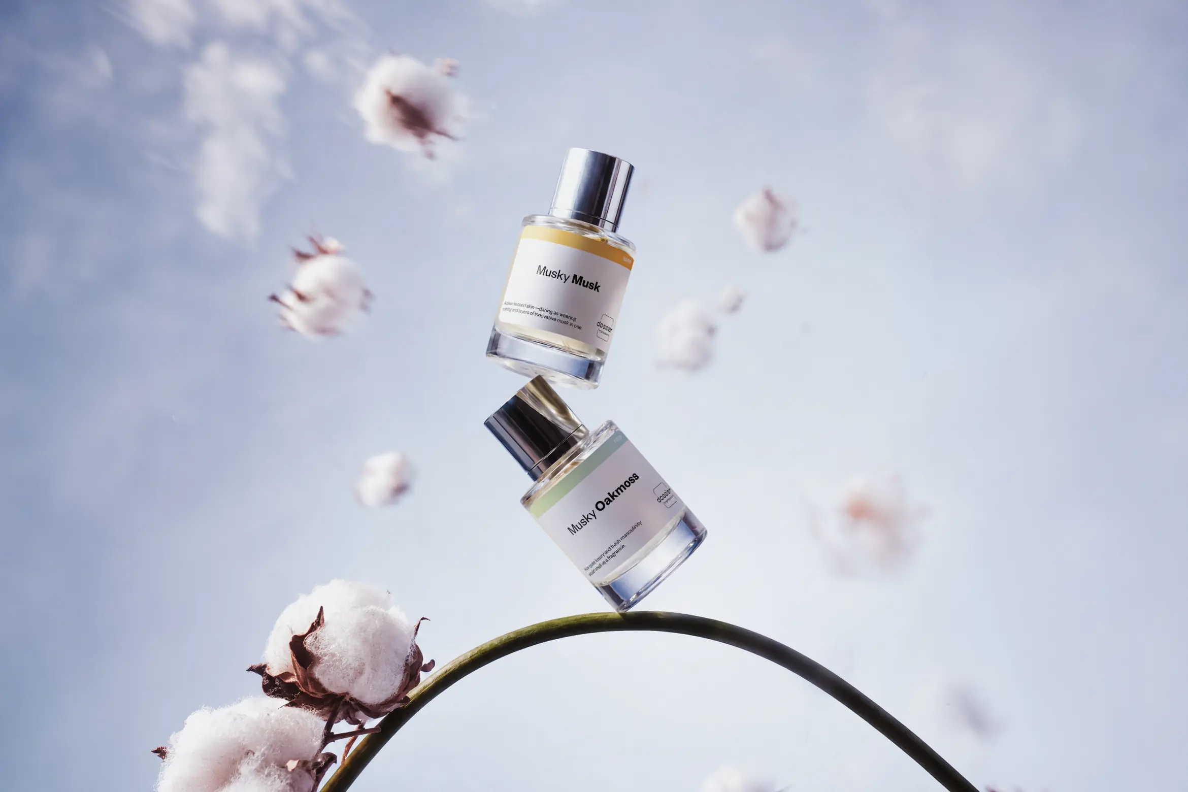 Two Dossier perfume bottles, Musky Musk and Musky Oakmoss, floating above cotton flowers against a soft blue sky.