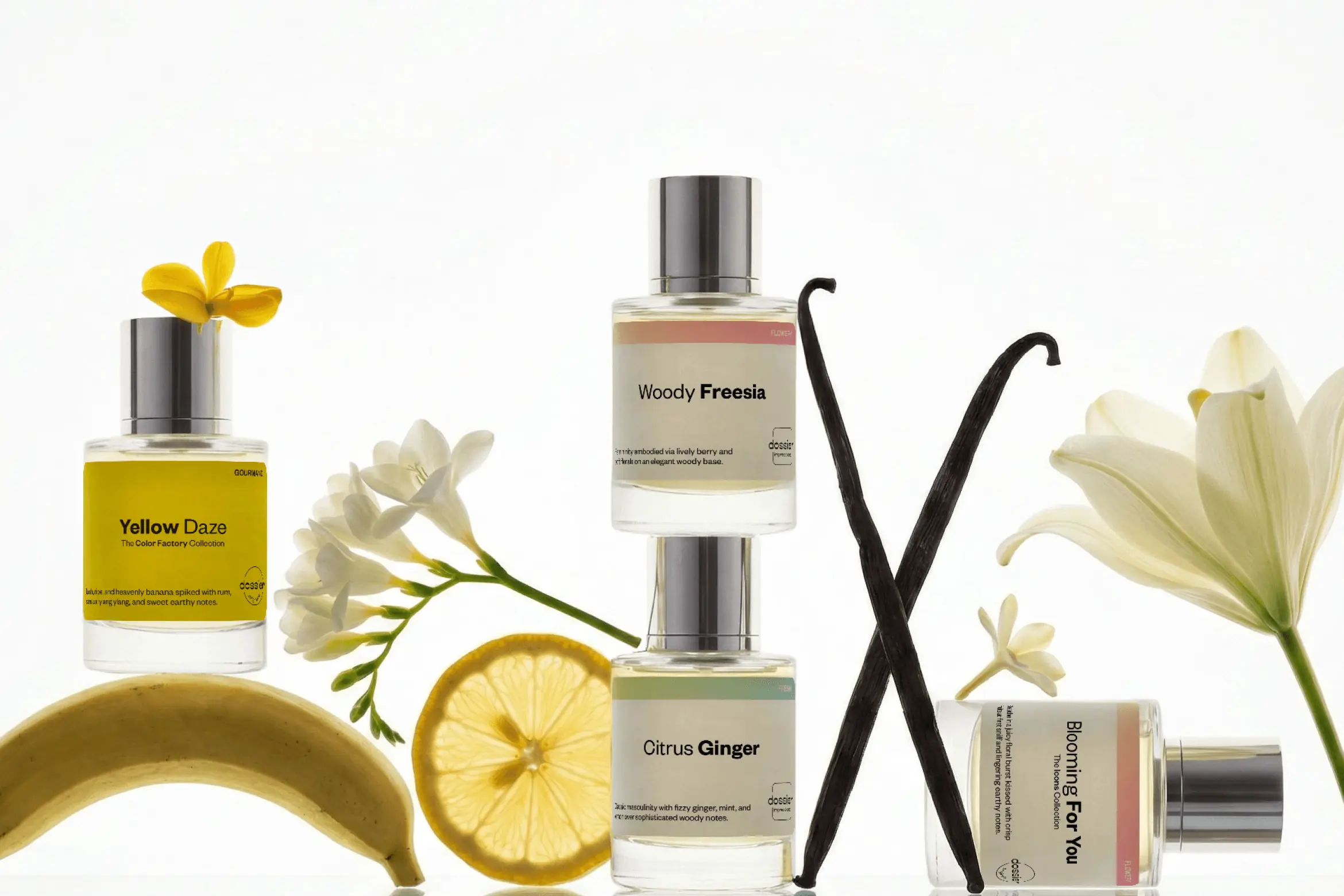 Perfume bottles including Yellow Daze, Woody Freesia, Citrus Ginger, and Blooming For You arranged with flowers, vanilla pods, lemon slice, and banana