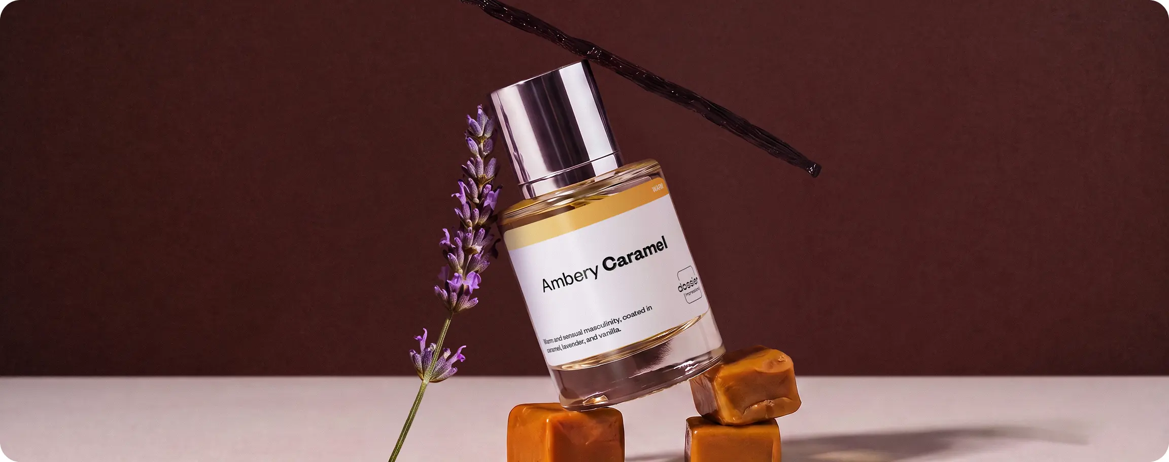 Dossier Ambery Caramel perfume bottle with lavender sprigs, caramel cubes, and a vanilla bean on a warm brown background